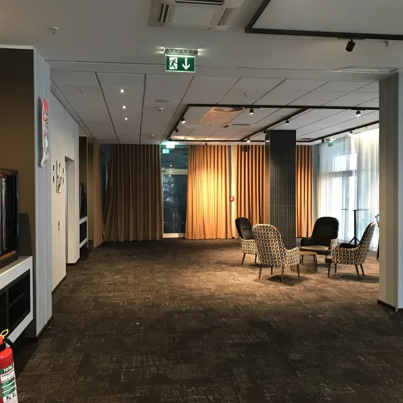 Heller Flur mit Sitzgruppe, braunen Vorhängen und Feuerlöscher vorne links.