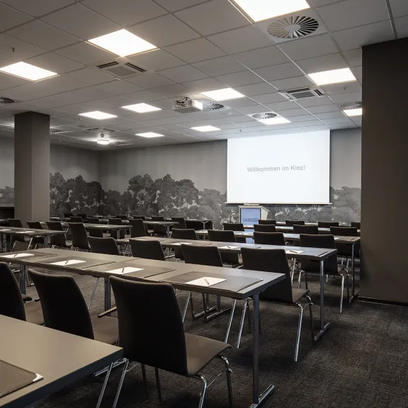 Konferenzraum mit leeren Tischen und Stühlen, Projektionsleinwand vorne