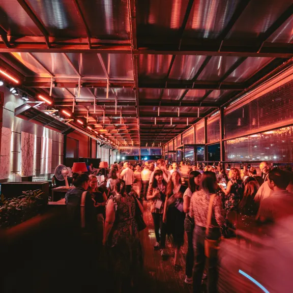 Menschen feiern nachts auf einer rot beleuchteten überdachten Terrasse.