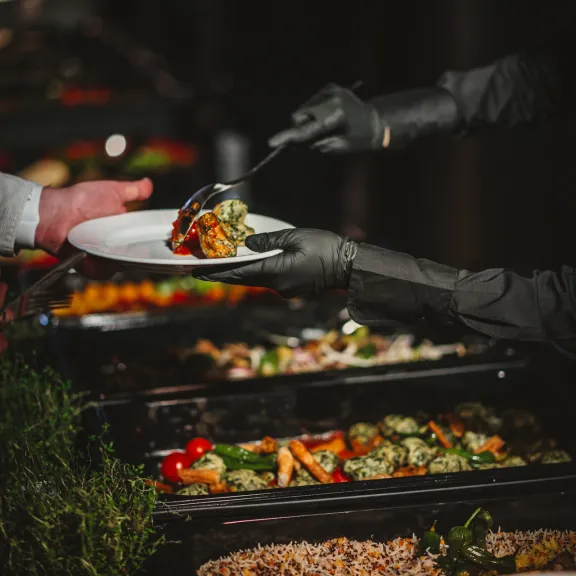 Buffet, Person serviert Essen mit Handschuhen auf einen weißen Teller.