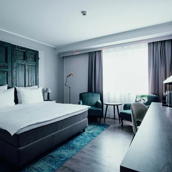 Modernes Hotelzimmer mit Doppelbett, Schreibtisch und Sessel am Fenster.