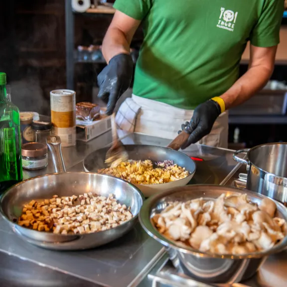 Koch bereitet Pilzgerichte in einer Küche zu, verschiedene Pilze in Pfannen.