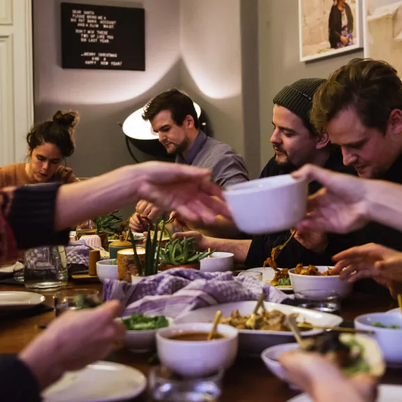 Mehrere Menschen sitzen gemeinsam essend an einem Tisch und teilen Speisen.