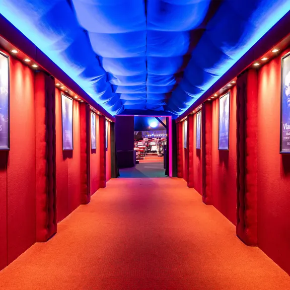 Roter Theaterflur mit blauer Beleuchtung und Showplakaten an den Wänden.