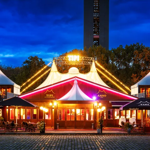 Beleuchtetes Theaterzelt mit weißen Zeltdächern und bunten Lichtern am Abend