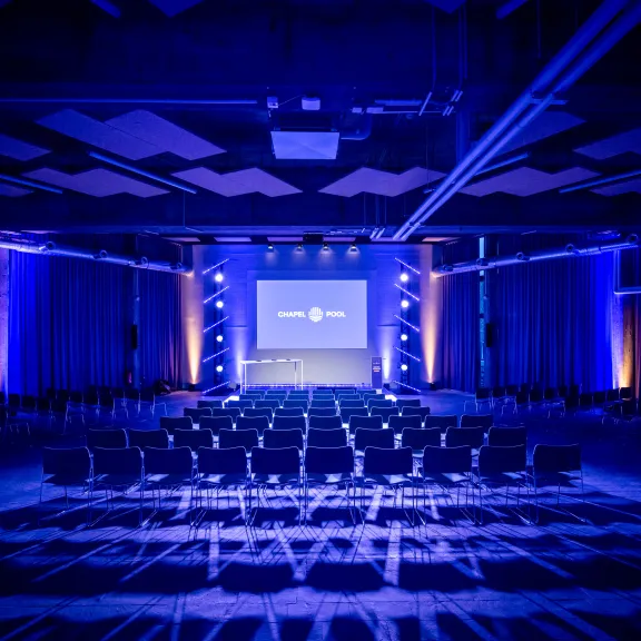 Leerer Konferenzsaal mit blauer Beleuchtung und Leinwand vorne