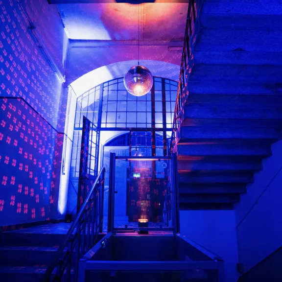 Blau-violett beleuchtetes Treppenhaus mit Discokugel und bunten Lichtmustern an der Wand.