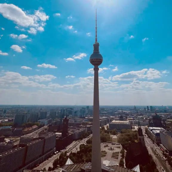 Fernsehturm Berlin vor blauem Himmel und Sonnenstrahlen, Stadt im Hintergrund.