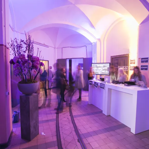 Menschen stehen in beleuchtetem Flur mit Blumenarrangement und Empfangstresen.