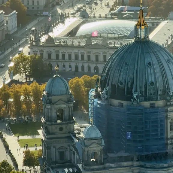Berliner Dom mit Kuppel im Sonnenlicht, umgeben von Bäumen und Gebäuden.