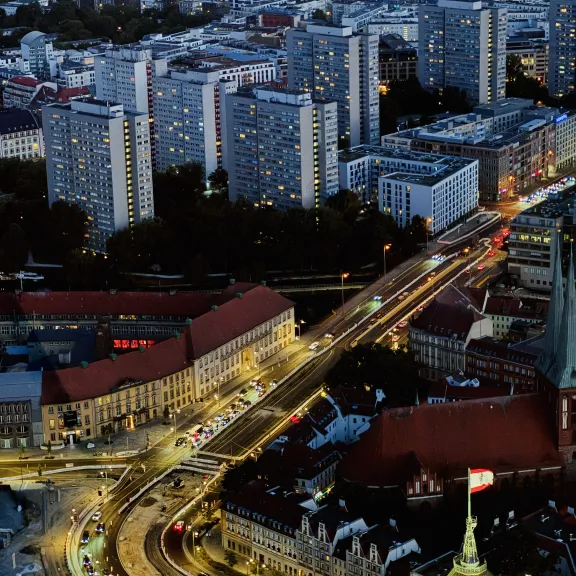 Stadtansicht bei Nacht mit beleuchteten Straßen und Hochhäusern im Hintergrund.