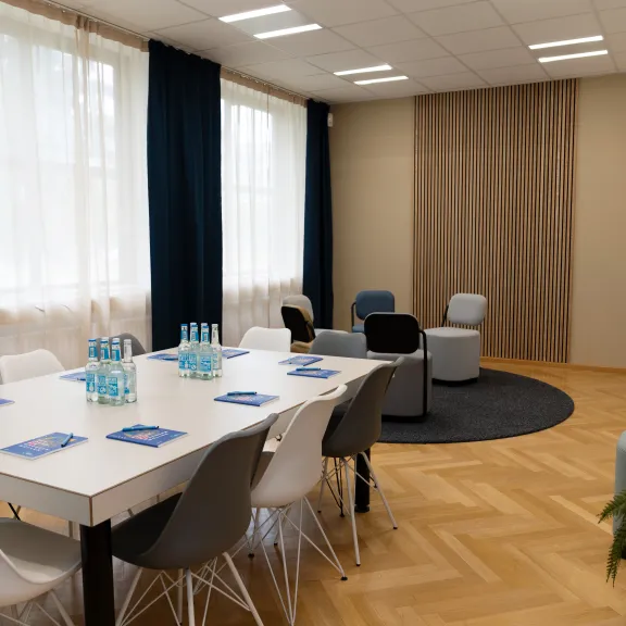 Moderner Besprechungsraum mit Tisch, Stühlen, Wasserflaschen und gemütlicher Sitzecke.