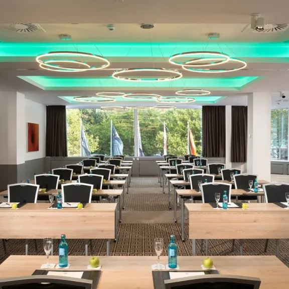 Konferenzraum mit Reihen aus Tischen, Stühlen und modernen Deckenleuchten.