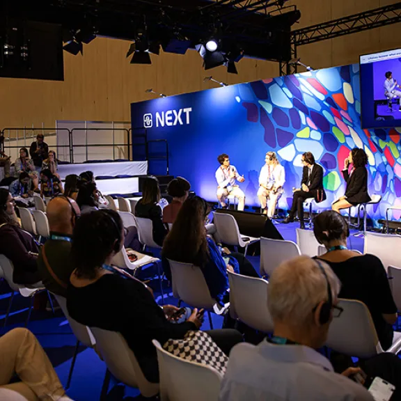 Podiumsdiskussion mit vier Personen auf einer Bühne vor interessiertem Publikum.