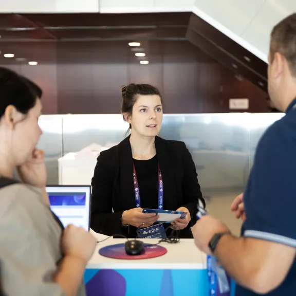 Frau am Empfangsschalter spricht mit zwei Personen.