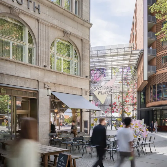 Straßenszene mit Café, Menschen gehen vorbei, Sitzplätze im Freien, sonnig