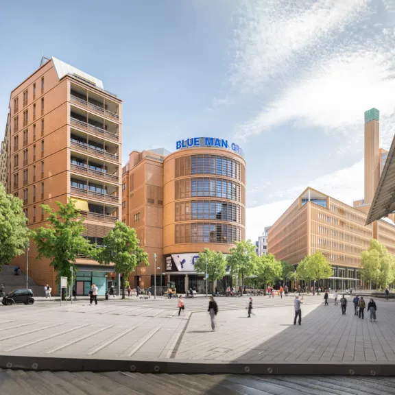 Weitläufiger Platz mit modernen orangefarbenen Gebäuden, Bäumen und Menschen bei Tageslicht.