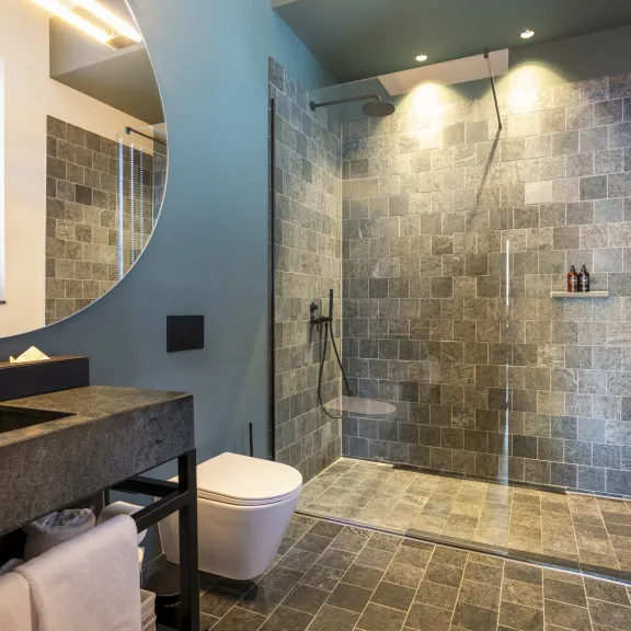 Modernes Bad mit großer ebenerdiger Dusche, dunklen Fliesen und Waschbecken.