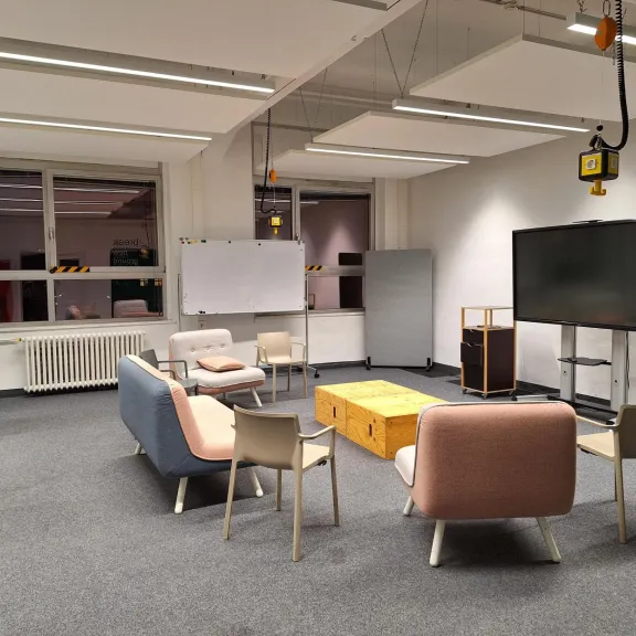 Heller Besprechungsraum mit Sofas, Stühlen, Whiteboard und großem Bildschirm.