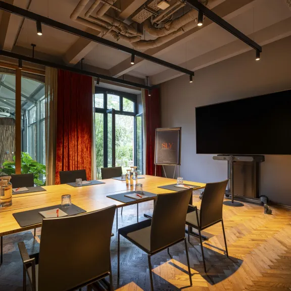 Moderner Konferenzraum mit großem Bildschirm, Holztisch und roten Vorhängen.