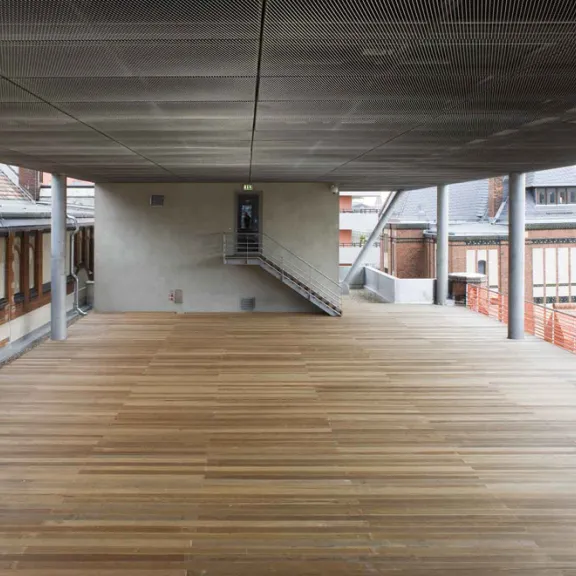 Überdachte Holzterrasse mit Blick auf moderne und historische Gebäude.
