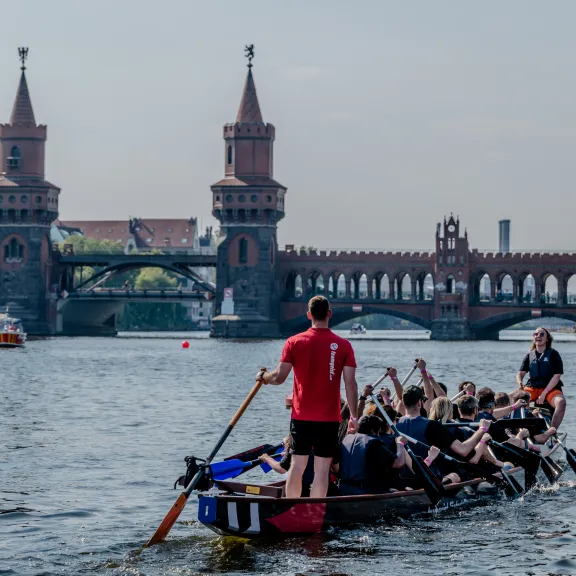 Drachenboot mit Team auf der Spree, im Hintergrund die Oberbaumbrücke in Berlin.