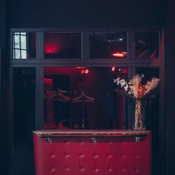 Roter Tresen mit Blumenvase, dunkler Raum im Hintergrund, dimmes rotes Licht.