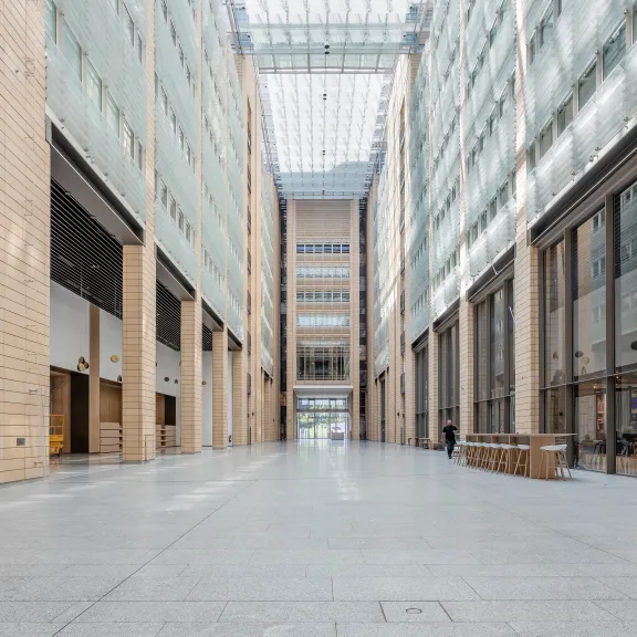 Helle, moderne Eingangshalle mit Glasdach und Holzverkleidung, wenige Möbel, leer.