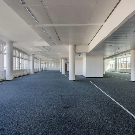 Leeres, modernes Großraumbüro mit Fenstern und blauem Teppichboden