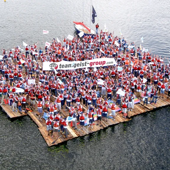 Große Menschenmenge auf Floß, hält Banner, schwimmt auf See.