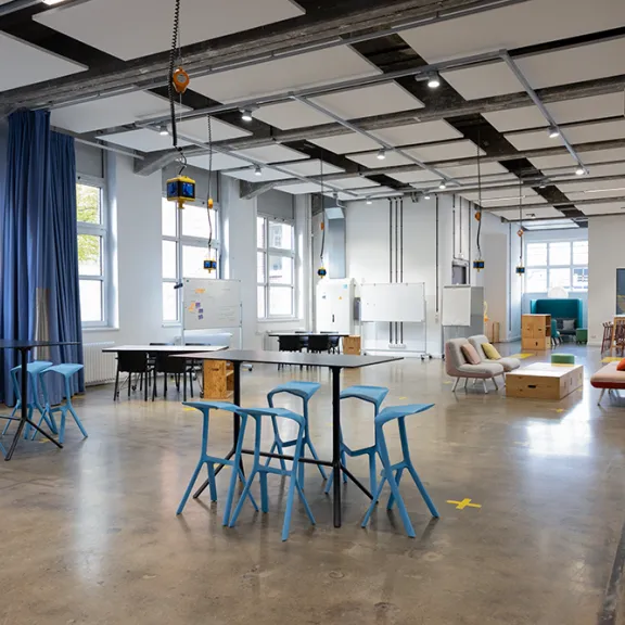 Heller, moderner Raum mit blauen Stühlen, Tischen und großen Fenstern