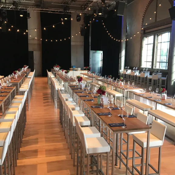 Festlich gedeckter Veranstaltungssaal mit langen Tischen, Stühlen und Lichterketten.