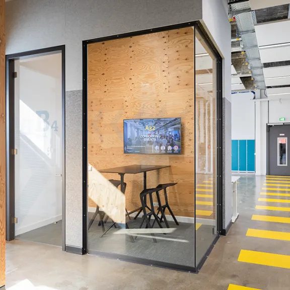 Kleiner Besprechungsraum mit Glastür, Holzwänden und wandmontiertem Bildschirm.