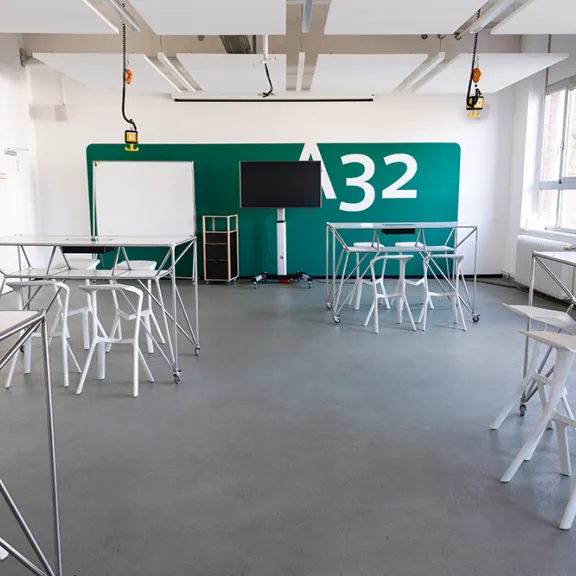 Heller Seminarraum mit Tischen, Stühlen und großem Monitor, grüne Wand mit "A32".