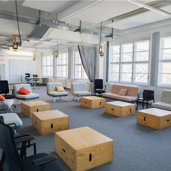 Moderner, heller Seminarraum mit Sofas, Stühlen und Holzwürfel-Tischen.