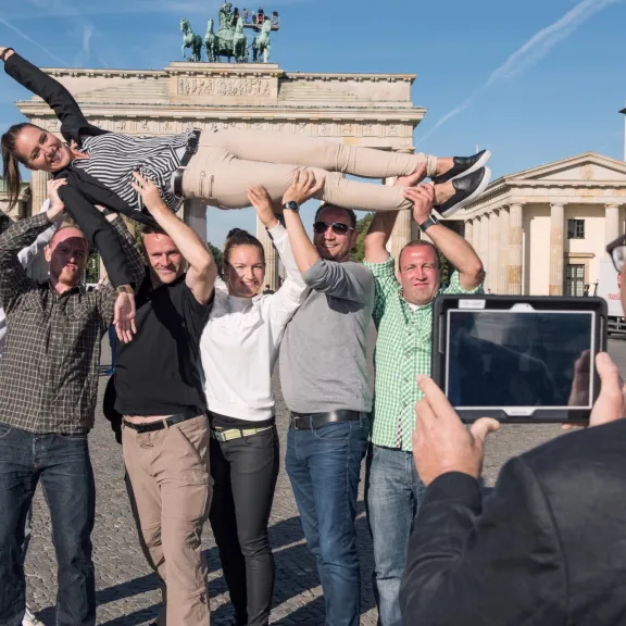 Gruppe fröhlicher Menschen posiert vor dem Brandenburger Tor für ein Foto.