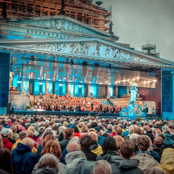 Großes Open-Air-Konzert vor beleuchtetem Gebäude, viele Menschen im Publikum.