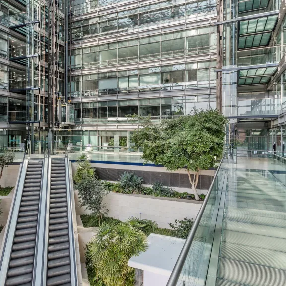 Modernes Bürogebäude mit Glasfassade, Rolltreppen und Innenbepflanzung.