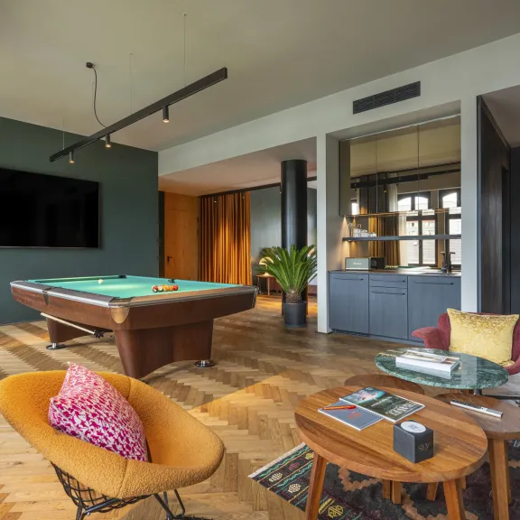 Modernes Wohnzimmer mit Billardtisch, großem Fernseher, bunten Sesseln und Holzmöbeln.