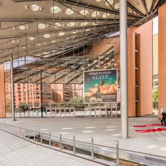 Moderne Glasfassade mit großem Vordach, Plakaten und rotem Teppich am Eingang.