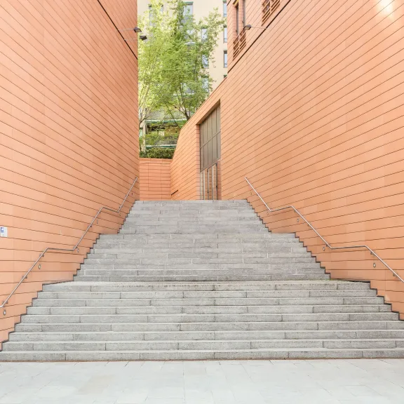 Breite Steintreppe zwischen orangefarbenen Gebäuden, oben grüne Bäume zu sehen.