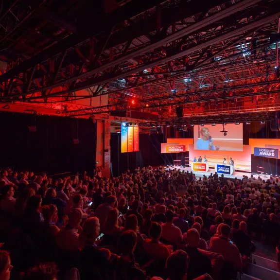 Großer Konferenzsaal mit gefüllten Sitzreihen und beleuchteter Bühne.