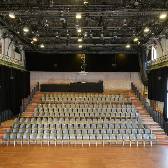 Leerer Veranstaltungssaal mit vielen Stuhlreihen und großer Bühne.