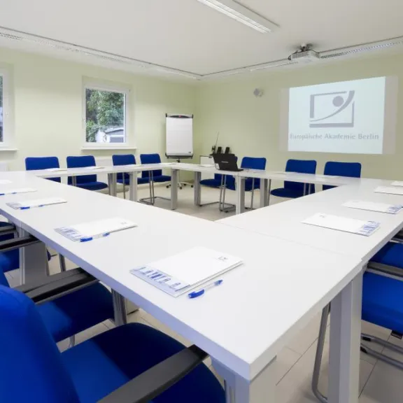 Konferenzraum mit U-förmigem Tisch, blauen Stühlen und Projektion an der Wand