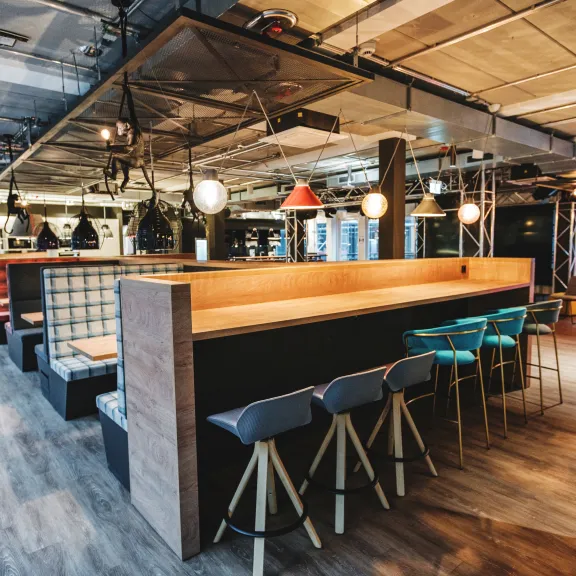 Moderne Veranstaltungsfläche mit Sitzbänken, Barhockern und stilvoller Beleuchtung.