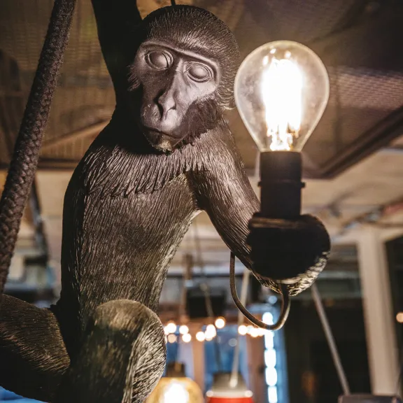 Affe-Skulptur hält eine leuchtende Glühbirne, Hängelampen im Hintergrund