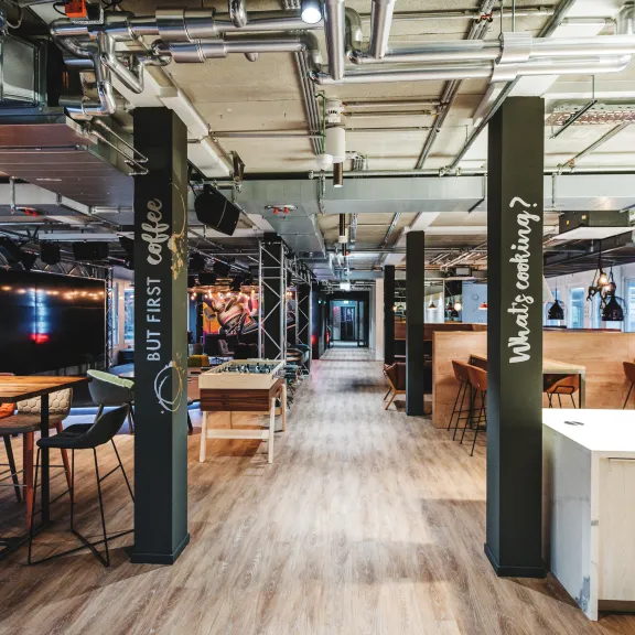 Moderne, offene Veranstaltungsfläche mit Holzboden, Arbeitsbereichen und Industrie-Decke