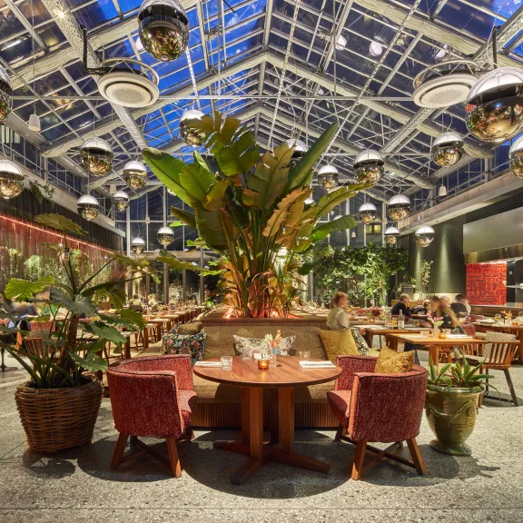 Modernes Restaurant mit Glasdach, vielen Pflanzen und stilvollen Sitzbereichen.