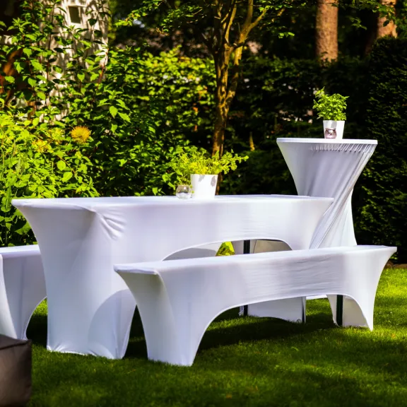 Gedeckter Tisch mit weißen Hussen im Garten, darauf kleine grüne Pflanzen.