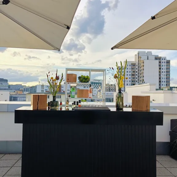 Moderne Bar auf Dachterrasse mit Sonnenschirmen und Stadtblick im Hintergrund.